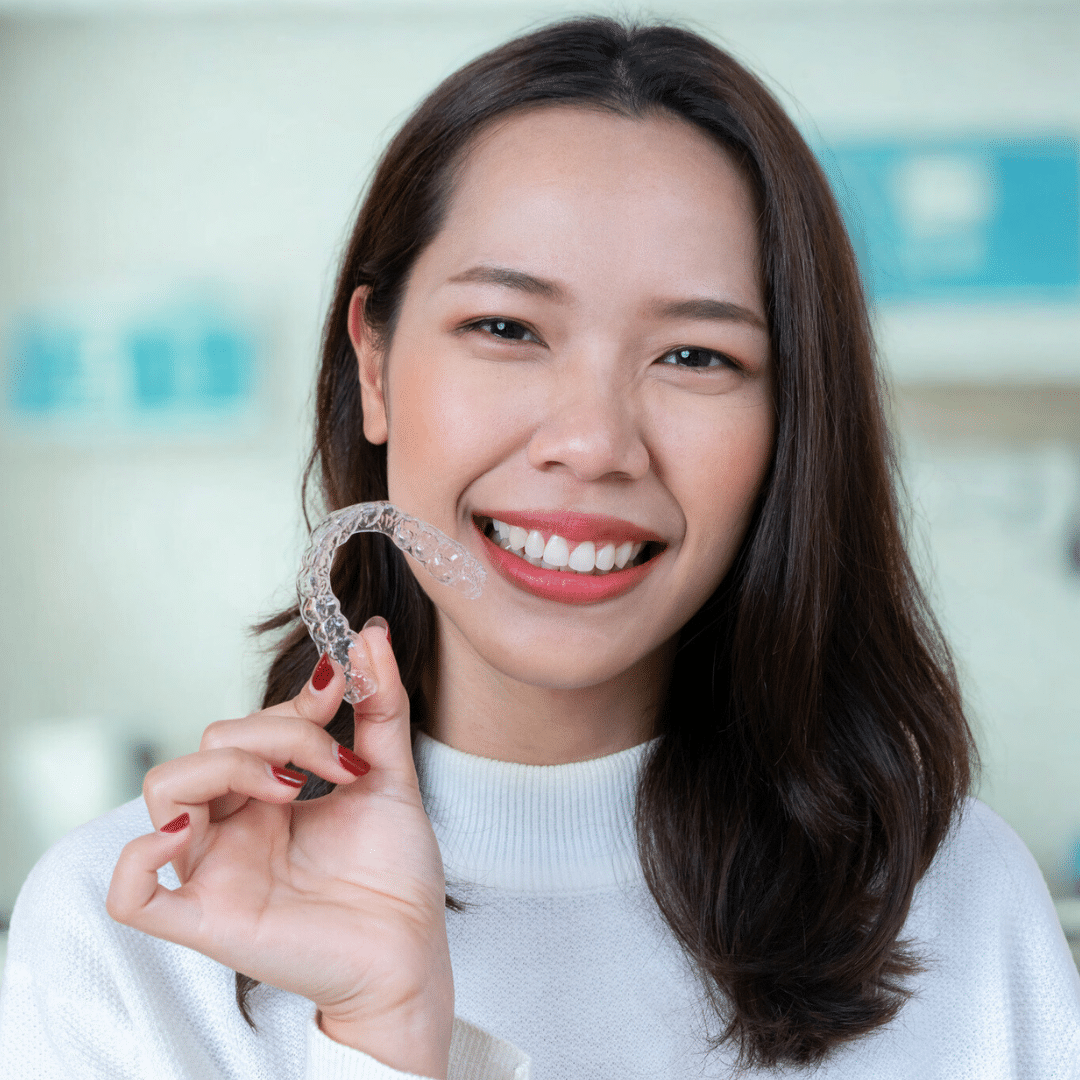 Smiling patient holding clear Invisalign aligner at Bernhardt & Smith Orthodontics, Bishop Drive Office and 50th Street Office in West Des Moines, IA